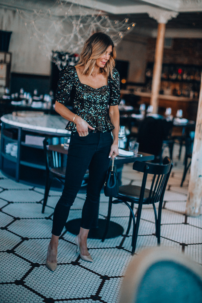 fashion blogger cella jane wearing black sequin holiday party top with black skinny jeans paired with nude heels